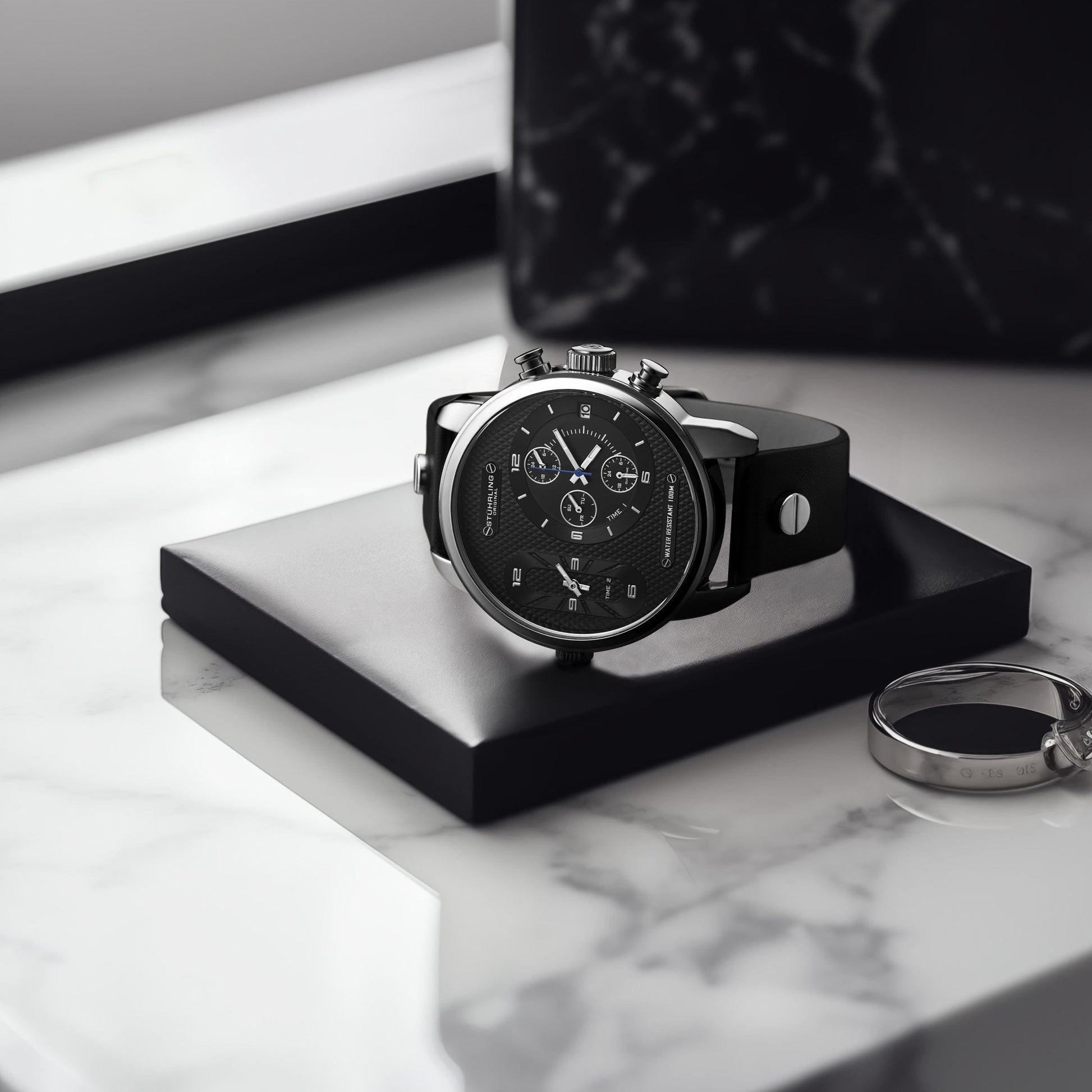 Black wristwatch on a white marble surface with a keychain.